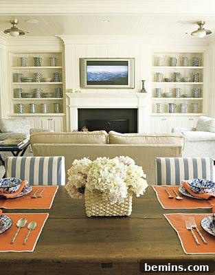 A TV unit with a fireplace below and racks on both sides, designed by House Beautiful, offers a functional and visually appealing entertainment center.