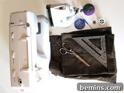 Sewing machine, iron, scissors, and ruler laid out on fabric, showcasing the necessary tools.