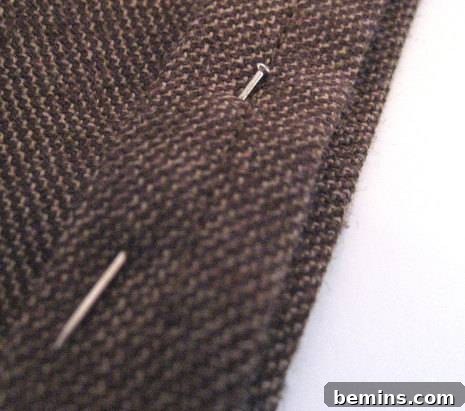 Close-up of a needle piercing the fabric, creating the final hem.