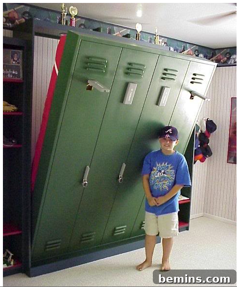 A young boy in a blue shirt and dark ball cap is standing next to green lockers that double as a pull down bed.