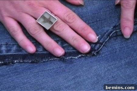 From Denim to Dream Skirt: A DIY Transformation 13 A person wearing a ring holds a seam on their jeans with their fingers, ensuring a smooth seam.