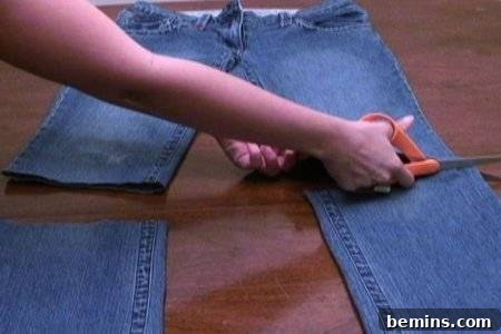 From Denim to Dream Skirt: A DIY Transformation 4 A person cutting the legs of jeans on a table with orange scissors, demonstrating the initial cut.