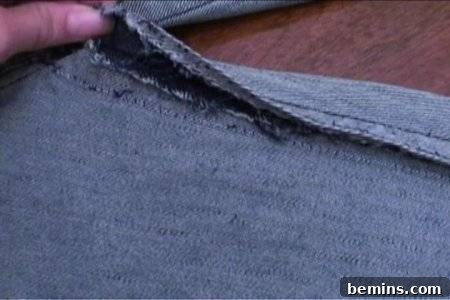 From Denim to Dream Skirt: A DIY Transformation 7 Stitching of a pair of blue jeans being raised up by a person with their hand on a table, showcasing the seam ripping process.