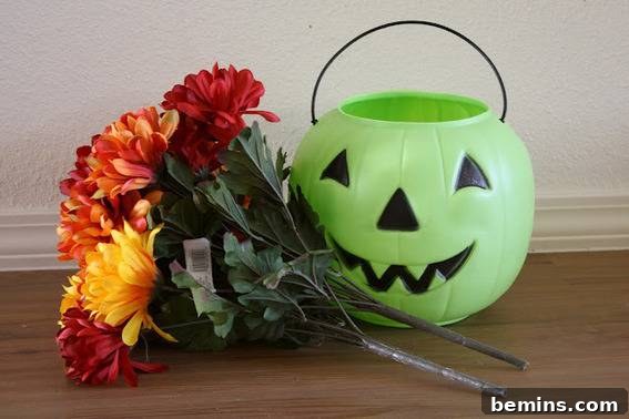 A green plastic jack o lantern near red and orange flowers.