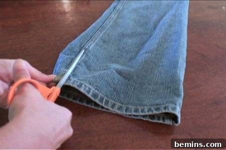 How to Sew Your Own Overalls 15 A person beginning to cut a pair of blue jeans by the leg seam.