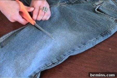 How to Sew Your Own Overalls 16 A person cutting a pair of jeans around the thigh area width-wise.