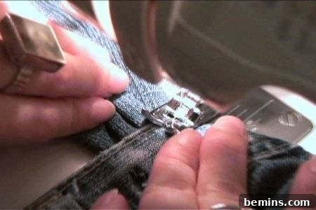 Hands guiding denim fabric as a sewing machine stitches the edge.