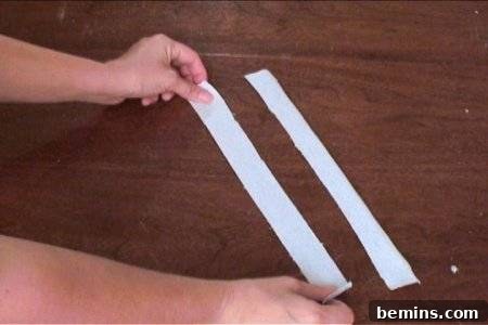 How to Sew Your Own Overalls 62 A pair of hands holding a strip of light-colored cloth by its ends alongside a matching piece of cloth.