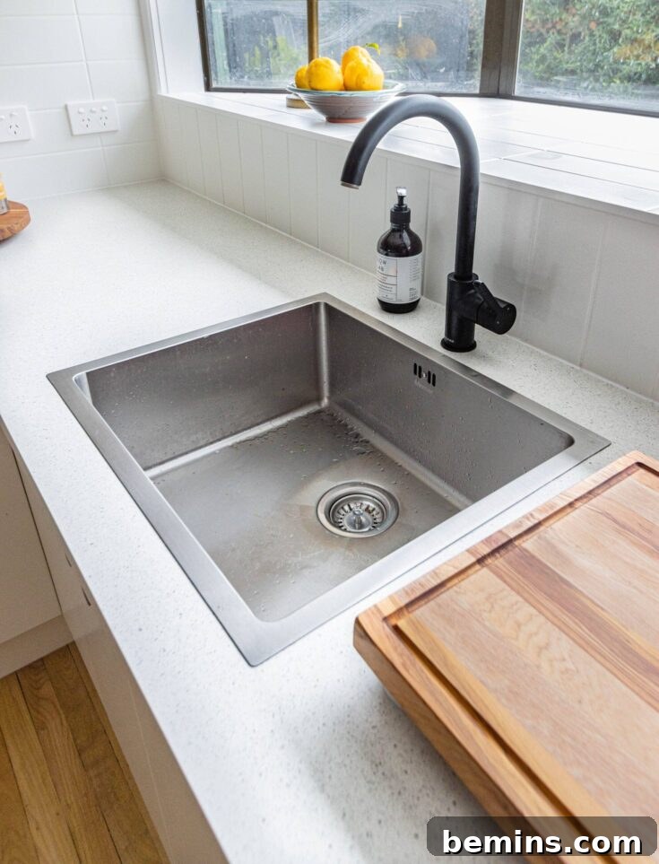 Close-up of a stainless steel sink being cleaned with a sponge.