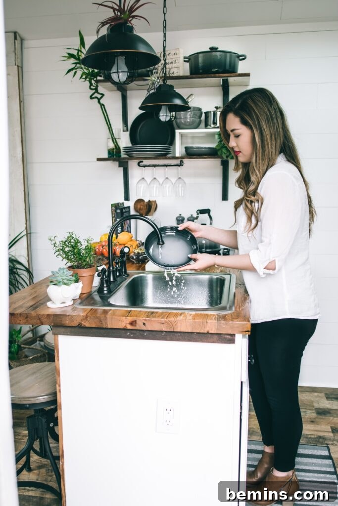 A woman diligently washing dishes in a clean and well-maintained stainless steel sink.