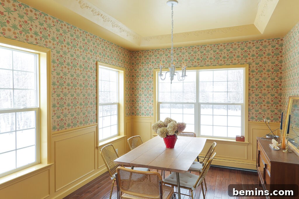 Dining area with brown dining tables and chairs, yellow wainscoting and yellow and blue wall paper with two large windows.