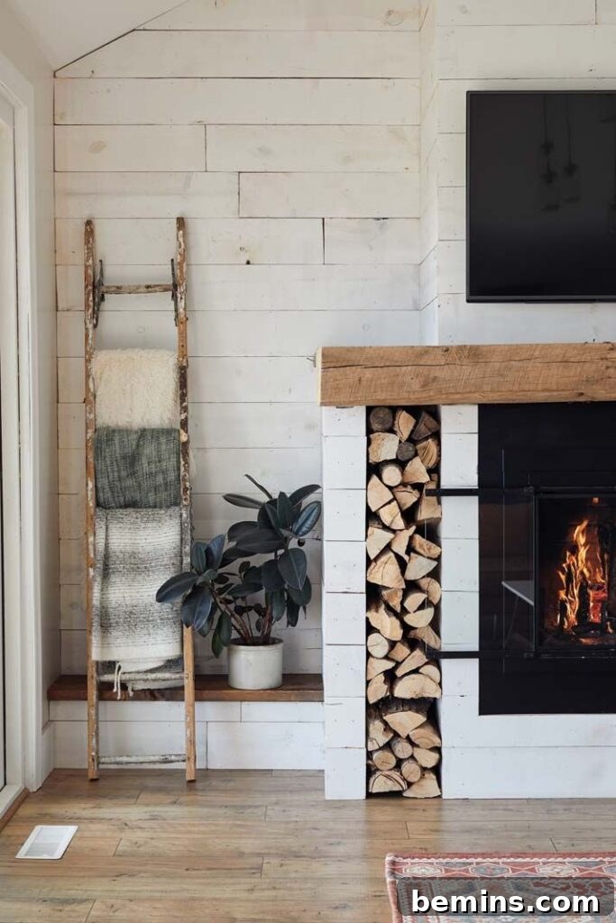 Spacious fireplace featuring a brown wooden mantel and stacked wood integrated into the wall to the left of the fireplace.
