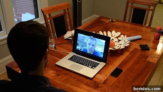 A person working on a laptop at a wooden dining table surrounded by natural light