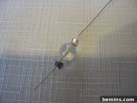 Thin piece of silver wire threaded with a large clear bead and two small silver beads.