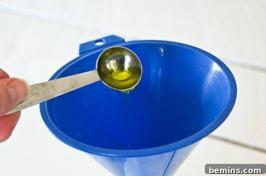 Pouring mild dish soap into an empty spray bottle using a funnel