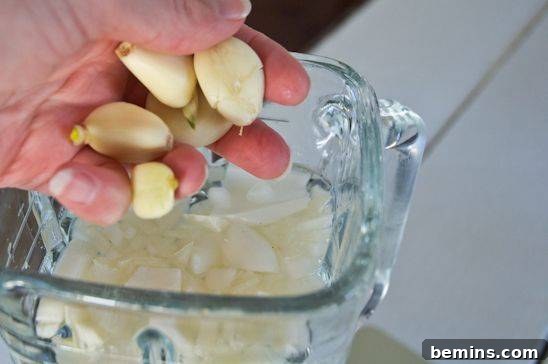 Adding peeled garlic cloves and quartered onion to the blender with warm water