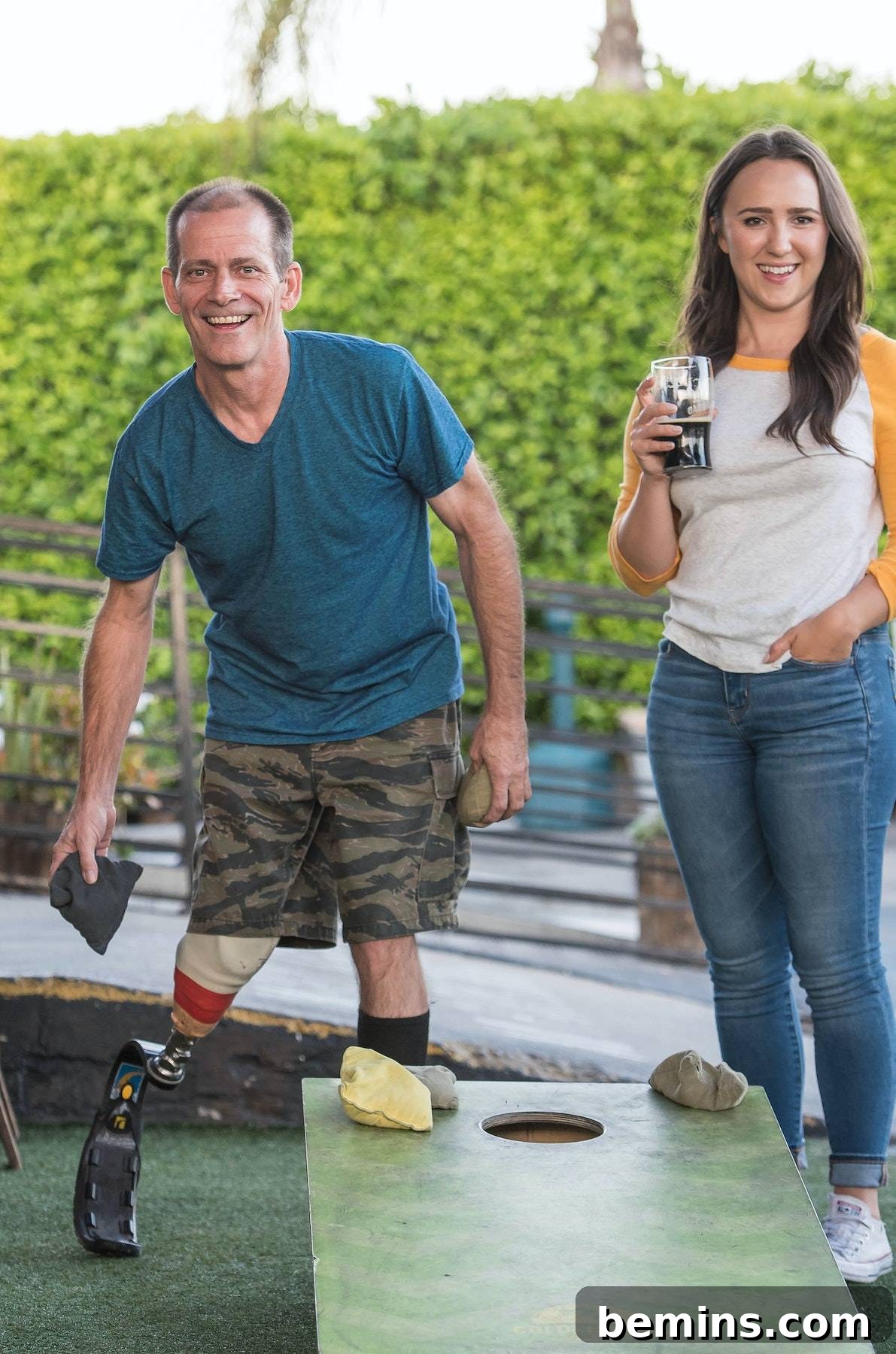 Hilarious Outdoor Games for Grown-Ups: Camping and Beyond 5 A man playing cornhole next to a woman holding a drink, enjoying a casual backyard game.