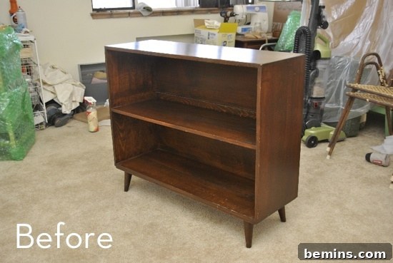 A brown wooden shelf sits in a messy room. The before image of a mid-century bookshelf renovation.