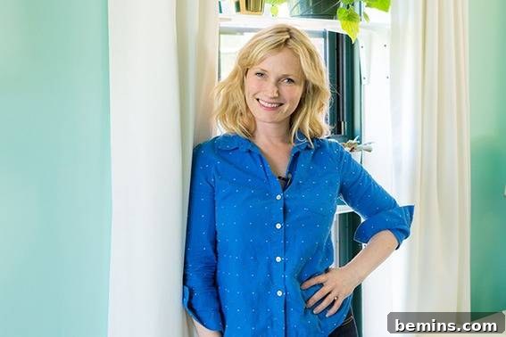 Fran Ferguson, a senior resident, leans against a window adorned with elegant white curtains in her newly designed, teal-painted room, exuding joy and contentment.