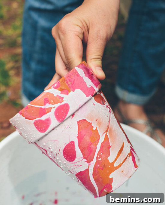 Hand holding a flower pot painted white with a pink and orange abstract design.