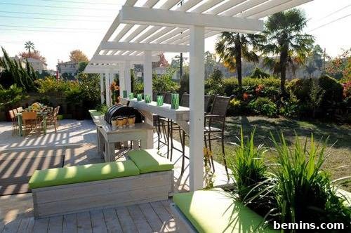 An inviting outdoor living space featuring a pergola covering a stylish bar area, adjacent to a large dining table with chairs, and various comfortable seating options on a well-designed patio.