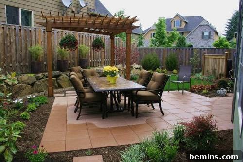 A thoughtfully designed small backyard patio featuring an outdoor dining table, surrounded by lush plants, with a charming pergola providing partial shade.