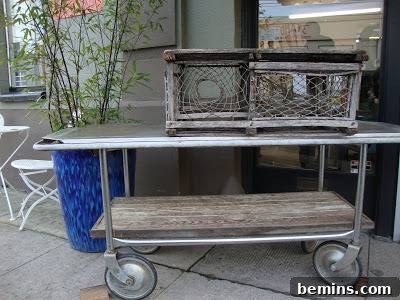 A cart with a silver top has a couple of wire mesh and wooden crates on top of it