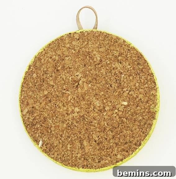 A circular piece of corkboard has a loop for hanging it at the top.