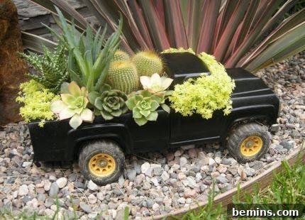 Miniature pickup truck filled with plants in a garden setting.