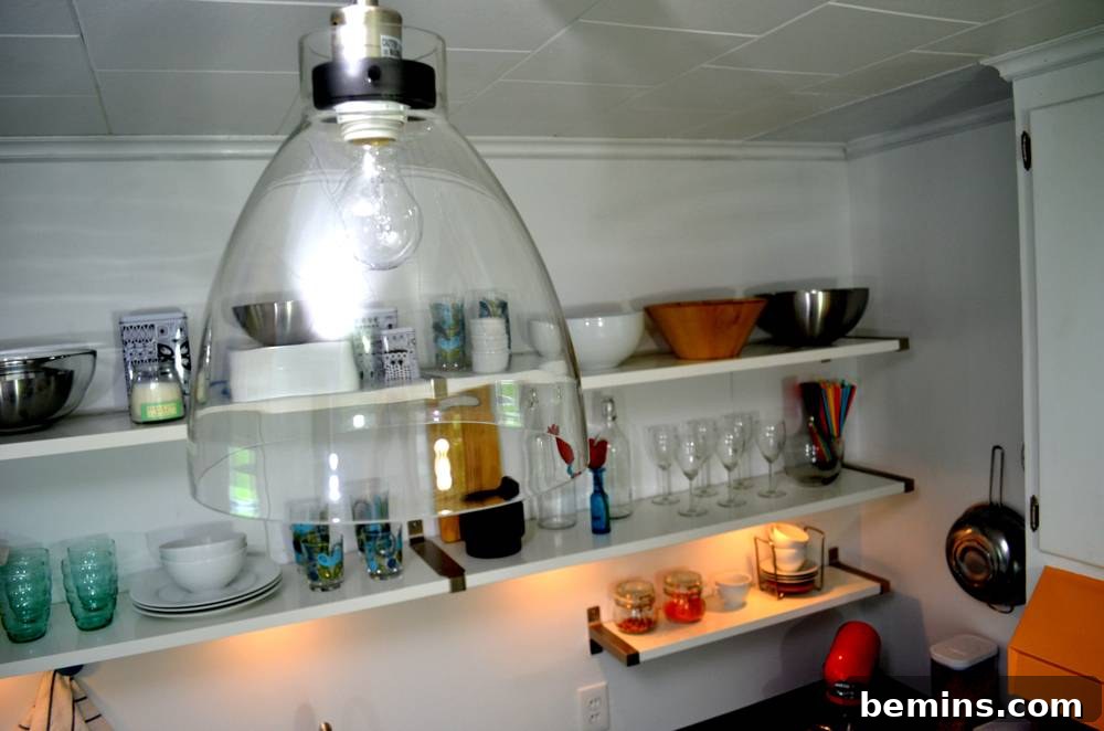 Open shelves holding glassware and serving bowls, illuminated by the new pendant light.