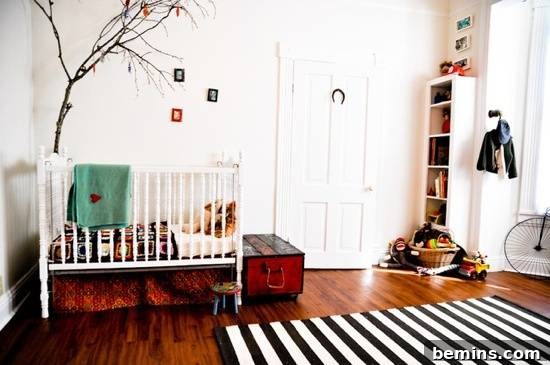 A serene nursery with a white crib nestled under a whimsical tree design, complemented by a wooden floor and a stylish black and white striped rug.