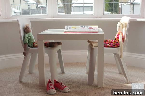 A kids' play table has two kid sized chairs pushed in with dolls sitting in them.
