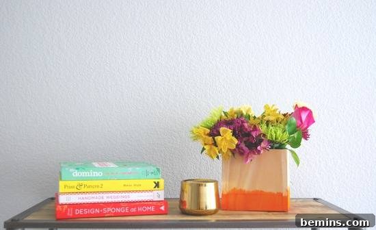 A table top with four books laying sideways, a gold cup and a peach bag with an orange bottom is filled with yellow, purple, green and pink flowers.