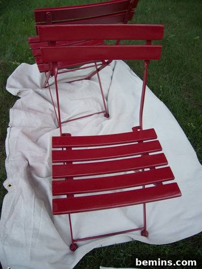 A red chair is sitting outside on a white piece of material. The first coat of glossy red paint.