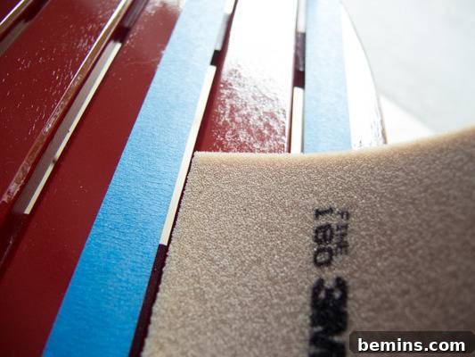 Sandpaper and painter's tape are on a wooden slatted chair that has been painted red. Smoothing out imperfections with a sanding pad.