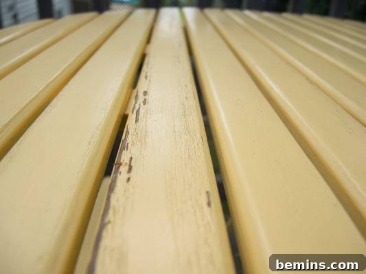 Close-up of light colored wooden slats showing peeling paint. A common problem with outdoor wooden furniture.