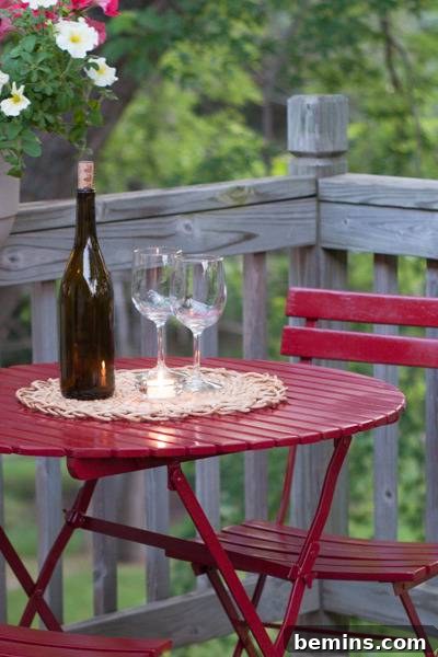 A red wood table that is on a porch with wine glasses and wine. Enjoying a glass of wine on the newly transformed bistro table.