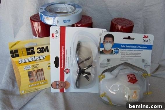 A set of packaged products, a mask, safety glasses, sandpaper, tape and spray paint bottles laying on a white cloth. All the essentials for a successful DIY project.