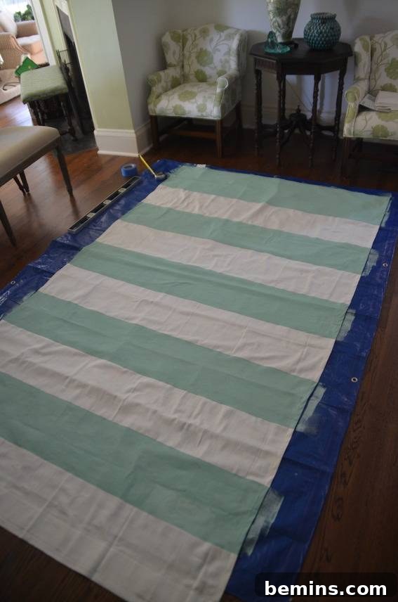 Painted Stripes: A Curtain Refresh 11 A green and white horizontally striped sheet on top of a blue blow up matress, showcasing the newly painted striped pattern after the tape has been removed.