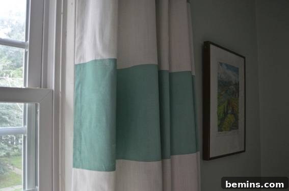Painted Stripes: A Curtain Refresh 13 A white curtain with a green broad horizontal stripe hangs on a white window, highlighting the clean and modern look of the DIY striped curtain.