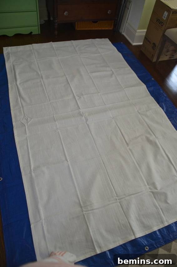 Painted Stripes: A Curtain Refresh 4 A piece of white cloth laid out on a blue plastic tarp, ready for measuring and taping in the DIY curtain process.