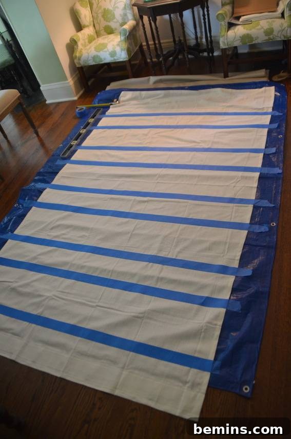 Painted Stripes: A Curtain Refresh 8 Blue tape is crossing a white material on a blue tarp, showcasing the taping process for creating the striped pattern on the curtains.