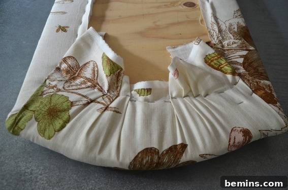 Green, brown, and beige cloth stapled to the underside of a seat, showing the upholstery work