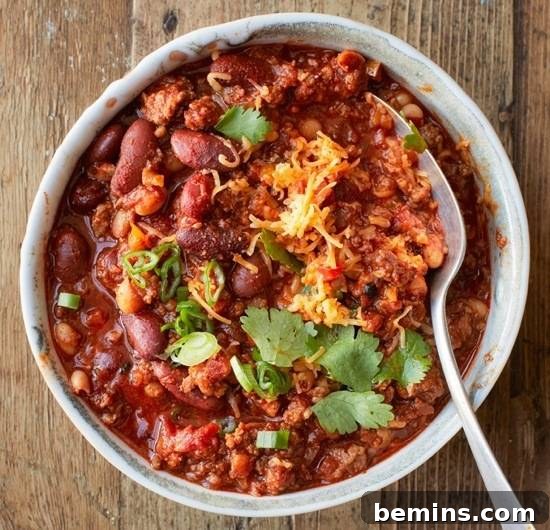 Chili with beans, cheese, and cilantro in a bowl with a spoon.