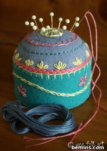 An exquisitely embroidered felt pincushion, skillfully crafted from a tuna can, holds sewing pins and a needle.