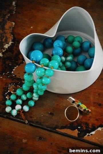 Blue beads are delicately arranged in a white, heart-shaped container crafted from an upcycled tuna can, resting on a rustic brown table.