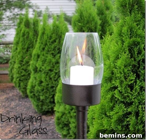 A beautifully crafted hurricane lamp, made from an upcycled tuna can, casts a warm glow near lush green plants.