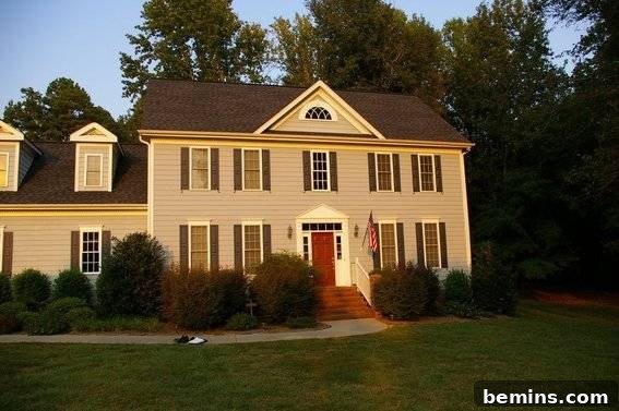 A two-story house proudly displaying an American flag near the front door, showcasing the patriotism and enhanced curb appeal achieved with a well-designed front porch