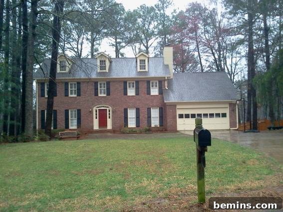 A mailbox standing sentinel in front of a three-story house nestled amidst pine trees, showcasing the potential for a front porch to enhance the overall aesthetic and curb appeal