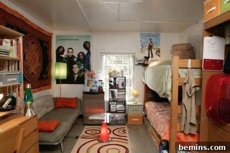 A bunk bed with unmade beds positioned next to posters and a couch inside a dorm room, creating a relaxed and lived-in atmosphere.